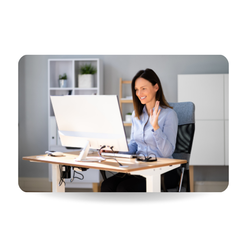 There is a woman sitting in front of a computer and waving at the screen 