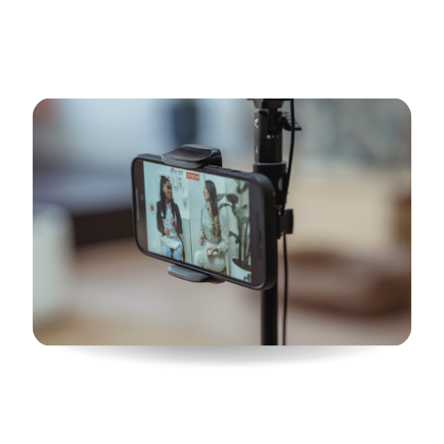 There is a mobile phone standing in a tripod recording an interview with two people