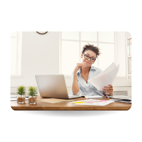 There is a girl sitting in a desk in front of a laptop and carrying some documents