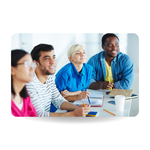 Four people are sitting around a table, pens in hand, smiling.